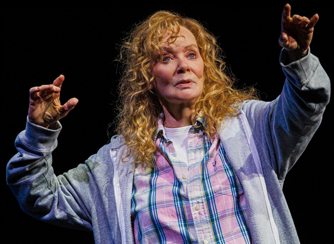 A person with curly hair and a grey sweatshirt with her hands up
Description automatically generated